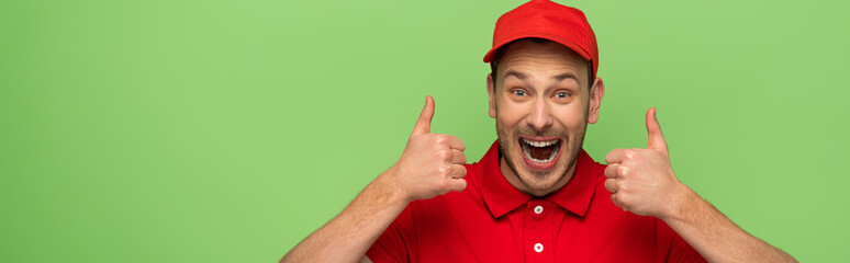 excited delivery man in red uniform showing thumbs up isolated on green, panoramic shot