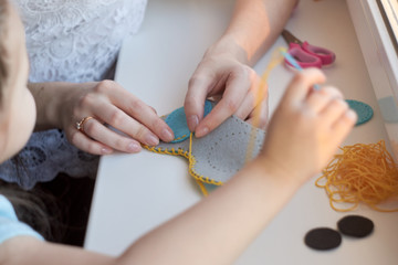 Сhild is sewing a toy owl from felt. Mother teaches the child to sew. 