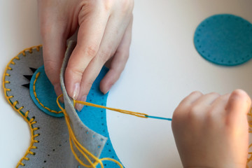 Сhild is sewing a toy owl from felt. Mother teaches the child to sew. 