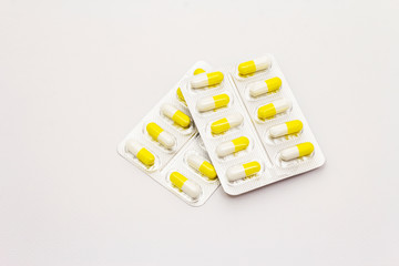 Pharmaceutical tablets, yellow white capsules in blister pack isolated on white background