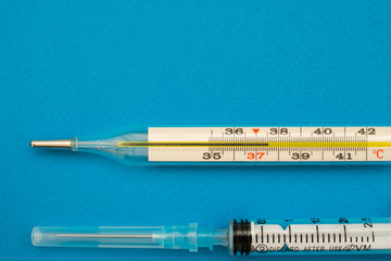 A thermometer and a syringe on a blue background. Heat. Copy space, C 37,5