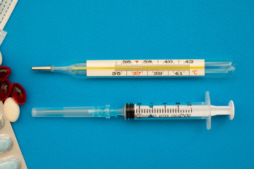 A thermometer and a syringe on a blue background. Heat. Copy space, C 37,5
