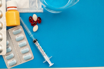 Medical examination and treatment concept. Red and white pills, thermometer, yellow serum, mask, a medical syringe on a blue background top view copy space. Medical flat lay