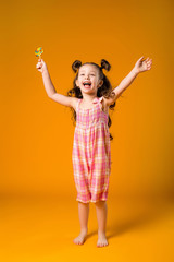 Adorable girl licking lollipop, on yellow background