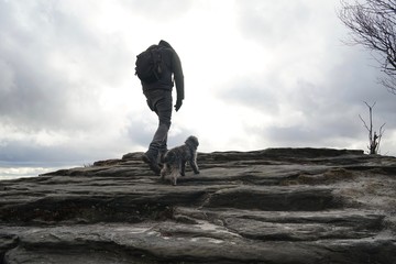 Silhouette of a man and its dog hiking together on a plateau against dramatic cloudy sky  