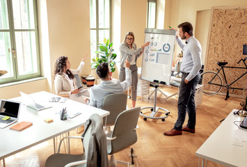 Obraz premium Group of young business people working together in office, two coworker conducting a business presentation using flip chart.