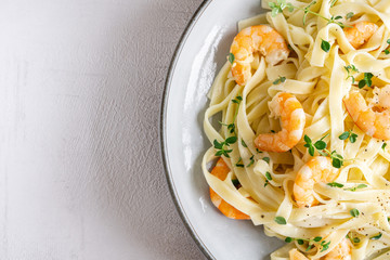 Italian pasta Tagliatelle in a creamy sauce with shrimp and persil on a plate, top view. Isolated. Copy space. Close up. Macro. Grey background. Concept: healthy food, tasty dinner. Top view. 