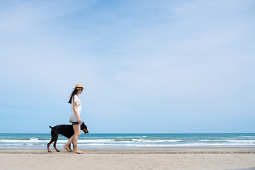 ビーチで散歩をするドーベルマンと女性