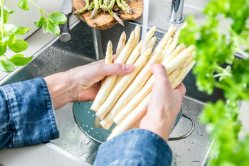 cropped shot of male hands in soil washing fresh asparagus in kitchen sink.