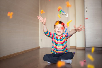 Fototapeta premium a cute, smiling red-haired boy in a multi-colored sweater plays a constructor, throws up and throws details