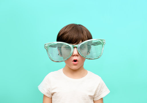 Cheerful little boy in big glasses express a surprised face isolated on blue background