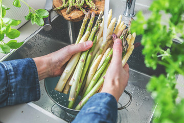 cropped shot of male hands in soil washing fresh asparagus in kitchen sink. - obrazy, fototapety, plakaty