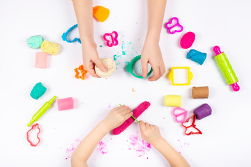 Little girls hands playing with colorful modeling clay on white background. Educational game with clay.