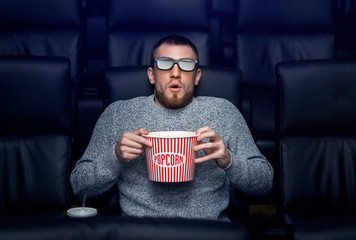 Alone in empty cinema. Frightened young man with popcorn watching 3D thriller in movie theater