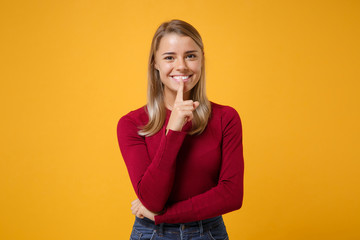 Smiling young blonde woman girl in casual clothes posing isolated on yellow orange wall background. People lifestyle concept. Mock up copy space. Saying hush be quiet with finger on lips shhh gesture.