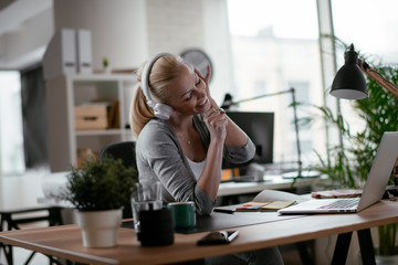 Portrait of businesswoman in office. Beautiful woman listening music at work.