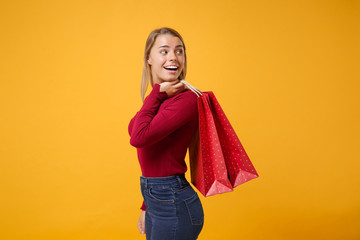 Side view of excited young woman girl in casual clothes isolated on yellow orange background. People lifestyle concept. Mock up copy space Hold package bag with purchases after shopping looking aside.