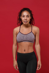 Fototapeta premium Beautiful young african american sports fitness woman in sportswear posing working out isolated on red wall background studio portrait. Sport exercises healthy lifestyle concept. Looking camera.