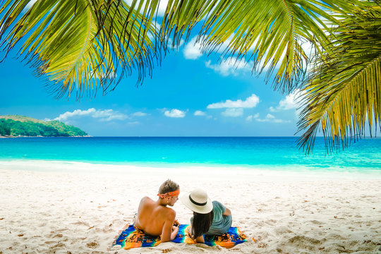Tropical white beach at Praslin island Seychelles, happy Young couple man and woman during vacation Holiday at the beach relaxing under a palm tree