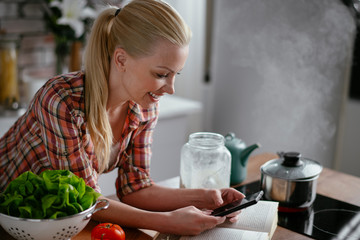 Beautiful woman in kitchen. Young woman writing message on phone.	