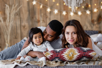 Portrait of a strong happy young family of positive african american dad young mother and mixed race little daughter resting together at home. Positive young family enjoying vacation with each other