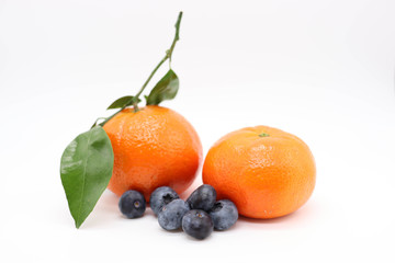 fresh tangerines with green leaves and black berries on white background