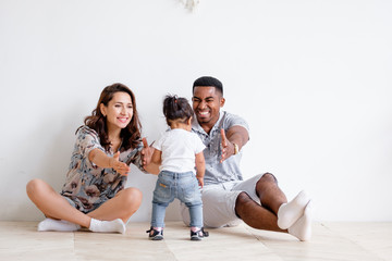 Beautiful young Caucasian woman couple and an African American man are pulling their hands to their charming mixed race daughter. Concept of posing on white background. Copyspace