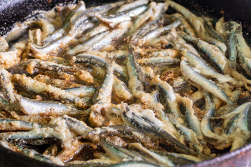 fried fish capelin on black frying pan