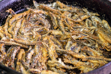 fried fish capelin on black frying pan