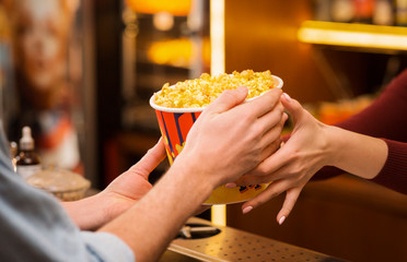 Young man buying popcorn from saleswoman in movie theater lobby, closeup of hands - obrazy, fototapety, plakaty