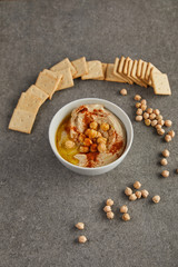 Bowl with tasty hummus, chickpea and crackers on grey