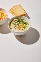 Bowls with tasty hummus and crackers on grey background