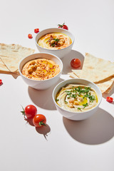 Bowls with delicious hummus, ripe cherry tomatoes and pita bread on grey background