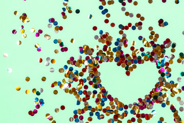 Heart shape made of golden colorful confetti splash on blue background. Festive backdrop of sparkles for birthday, valentine's day, carnival