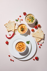 Top view of plates and bowls with hummus, fresh vegetables and pita bread on grey background