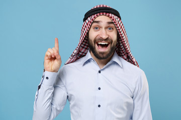 Excited bearded arabian muslim man in keffiyeh kafiya ring igal agal casual clothes isolated on pastel blue background. People religious lifestyle concept. Holding index finger up with great new idea.