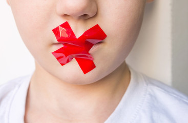 Young child with mouth sealed with red duct tape. Domestic violence and child protection, concept.