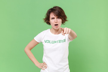 Strict angry young brunette woman in white volunteer t-shirt isolated on pastel green background....