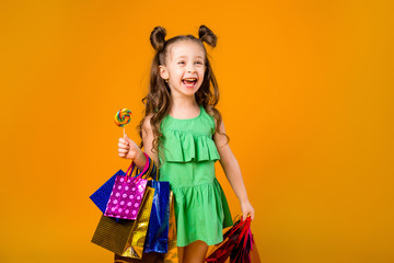 child girl smiling holding colorful shopping bags, standing on a yellow background. little fashionista, space for text
