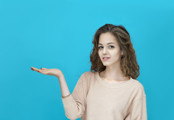 Portrait of a young beautiful woman wearing sweatshirt showing anything on her palm and looking at you isolated over blue background