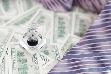 Drop of black oil of Brent brand in crystal cube on background of hundred dollars bills,tie of...