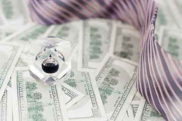 Drop of black oil of Brent brand in crystal cube on background of hundred dollars bills,tie of...