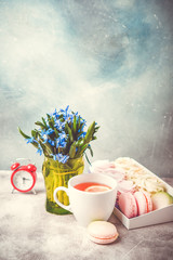 Early morning breakfast vertical background. Macaroons, flowers and alarm clock on the table.