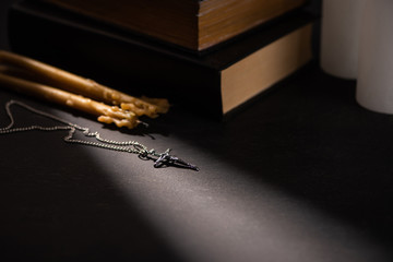 cross and church candles near holy bible on black dark background with sunlight