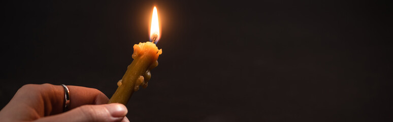cropped view of woman holding burning church candle in dark, panoramic shot
