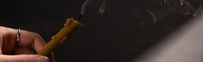 cropped view of woman holding extinct candle in dark, panoramic shot