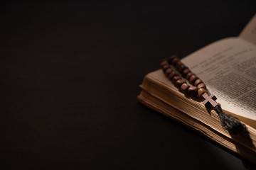holy bible with catholic rosary in dark with sunlight