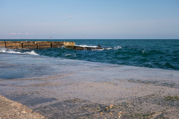 Restless sea, concrete pier, waves, seagulls.