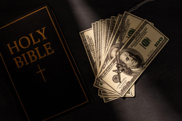 top view of holy bible with money and cross on dark background with sunlight