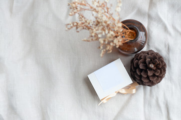 Small square diamond ring box, tied with cream colored ribbon With pine cones placed beside the box Adorned with dried flowers in a brown glass bottle Put on a light brown fabric